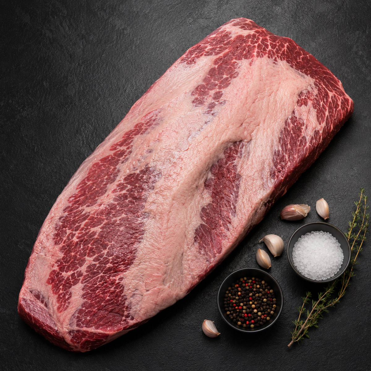 Raw beef brisket on a dark surface with spices and herbs.